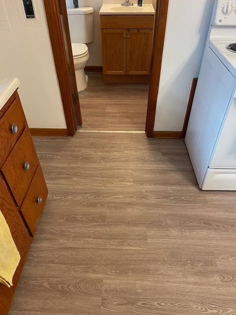 A bathroom with a wooden floor , a toilet , a sink , and a stove.