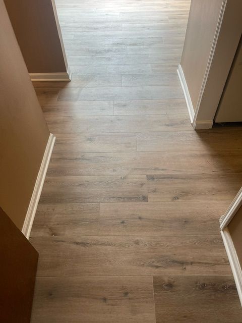 A hallway with a wooden floor and a doorway leading to a kitchen.