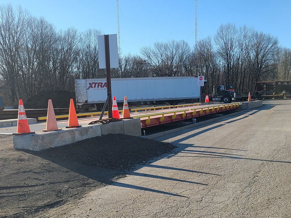 A truck is driving down a road next to a scale.