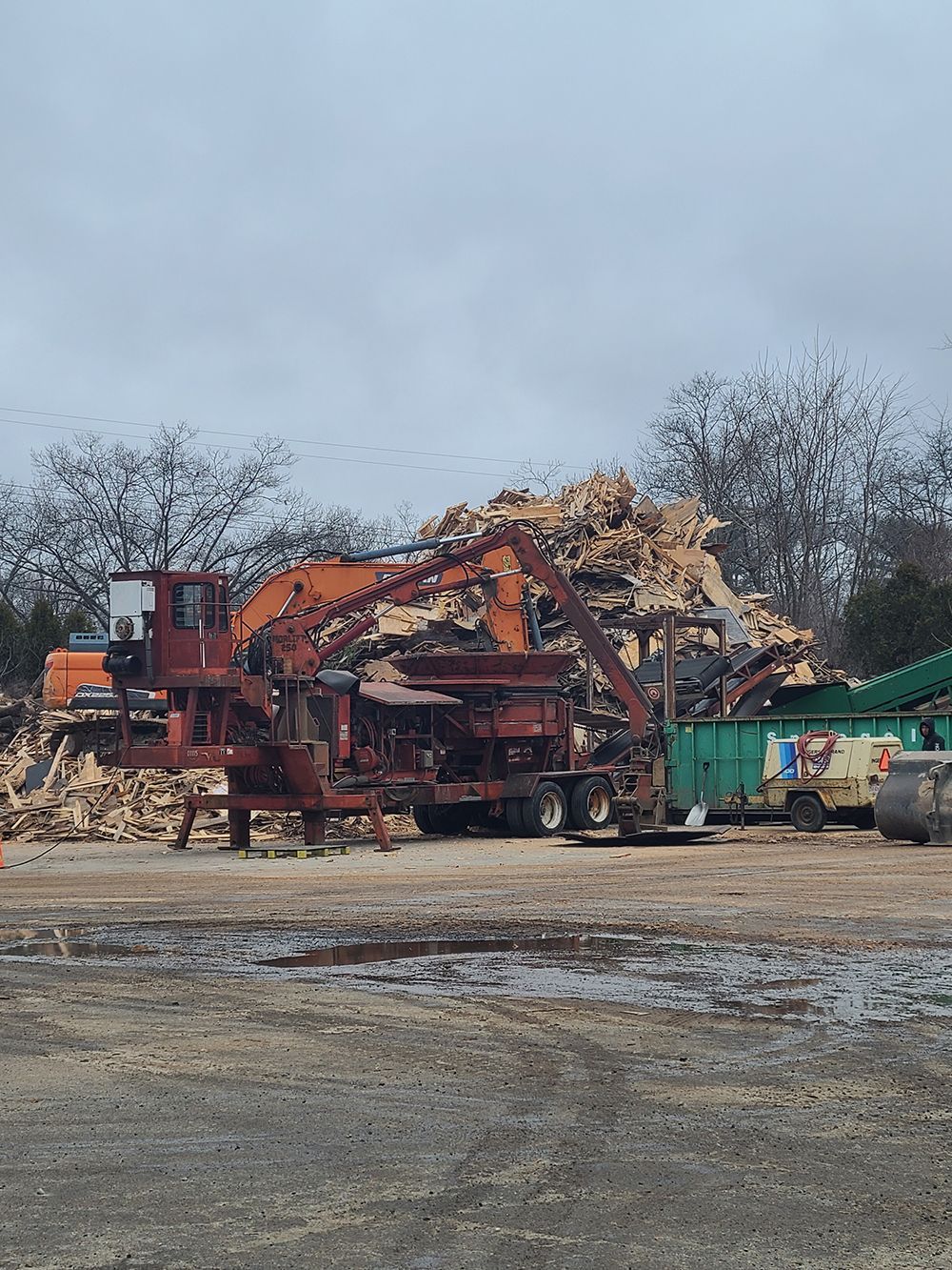A large pile of wood is being processed by a machine in a field.