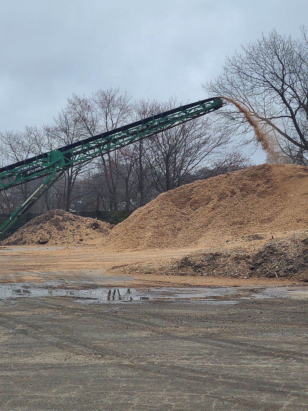A conveyor belt is moving a pile of wood chips in a field.