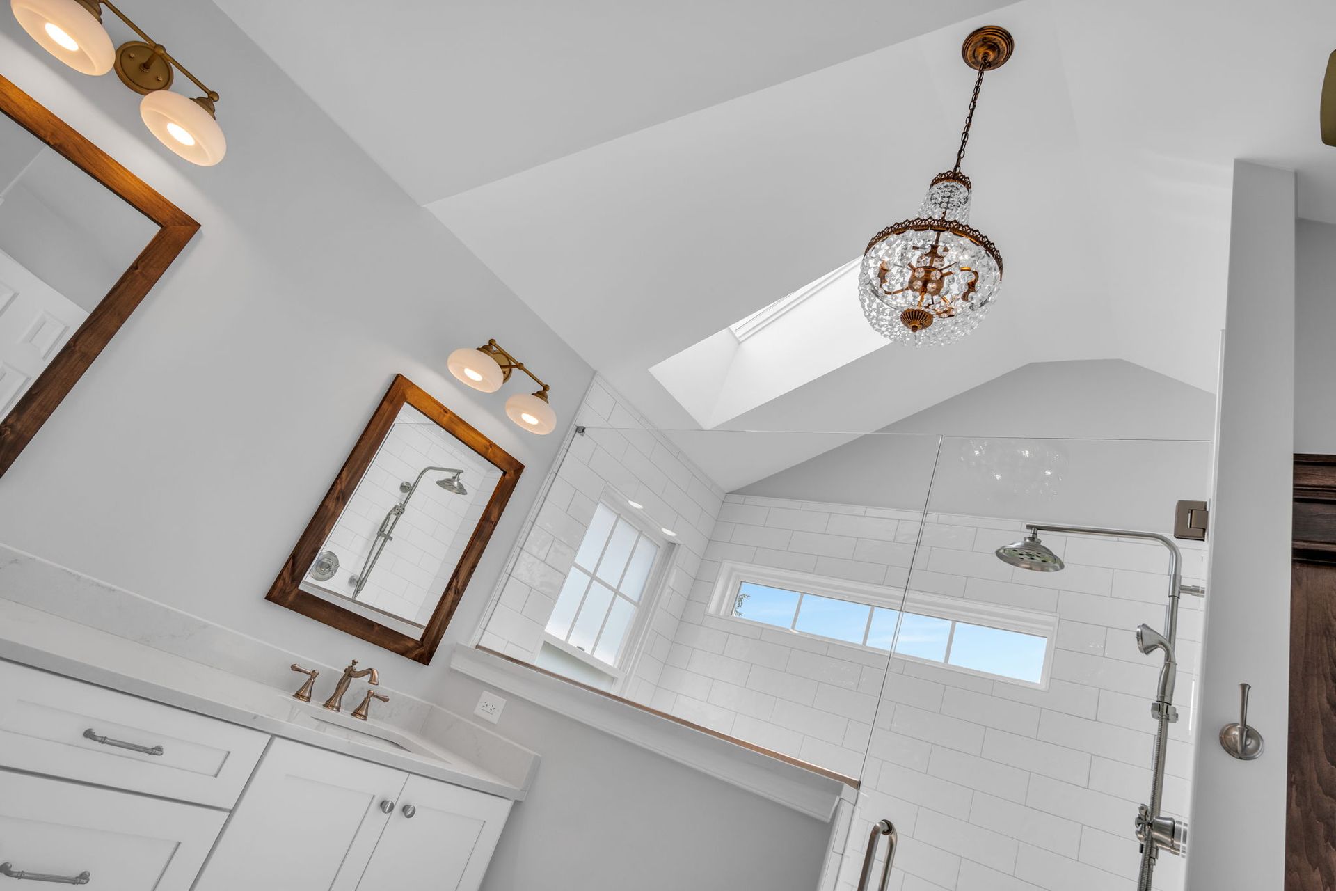 A bathroom with a walk in shower , sink , mirror and skylight.