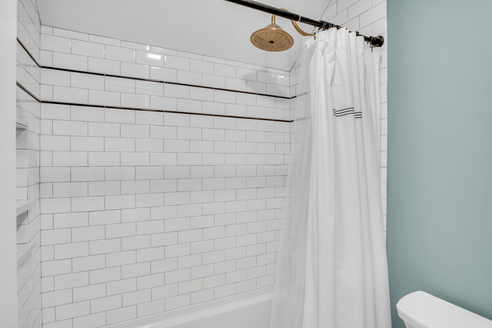 A bathroom with white tiles and a shower curtain