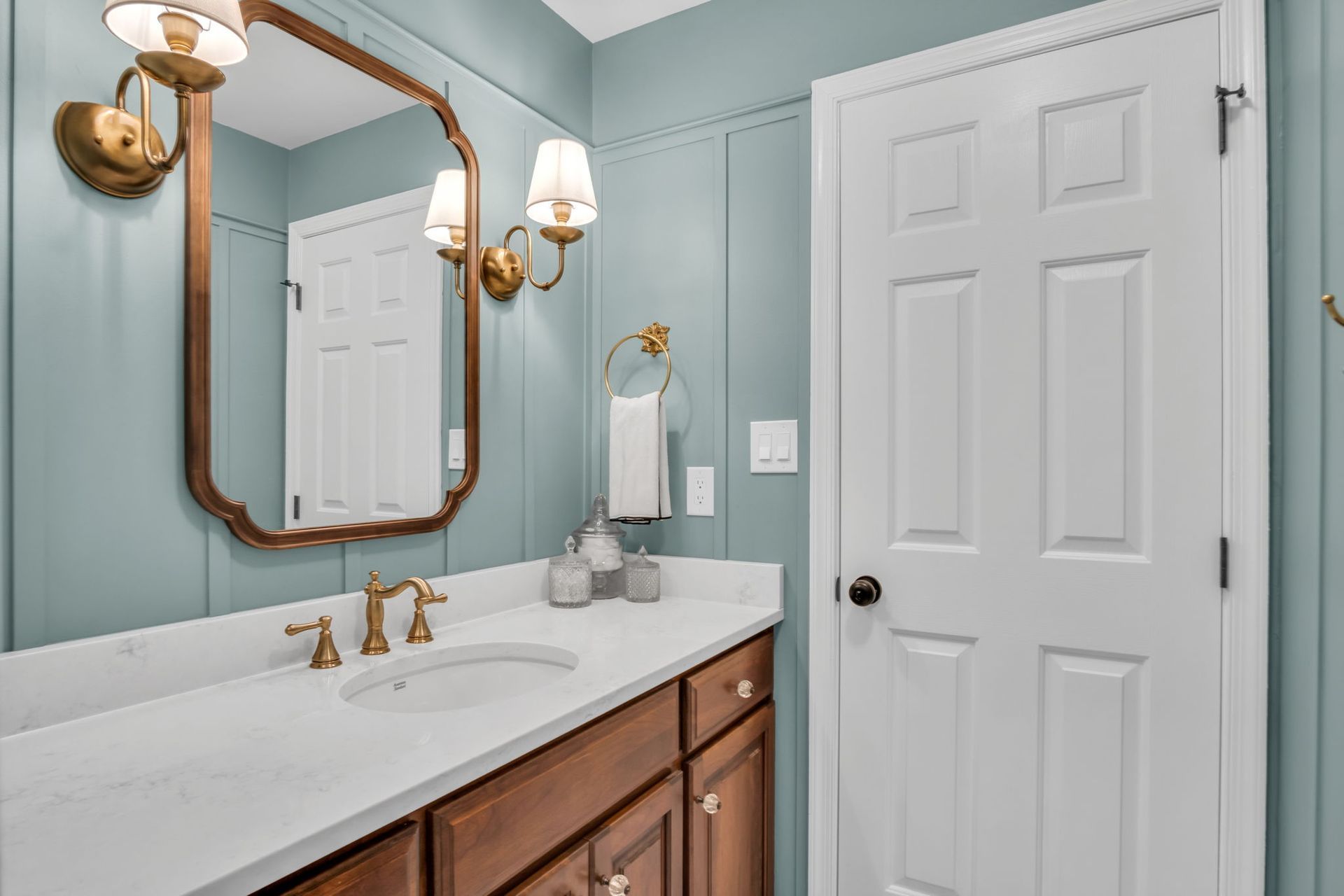 A bathroom with a sink , mirror , cabinets and a door.