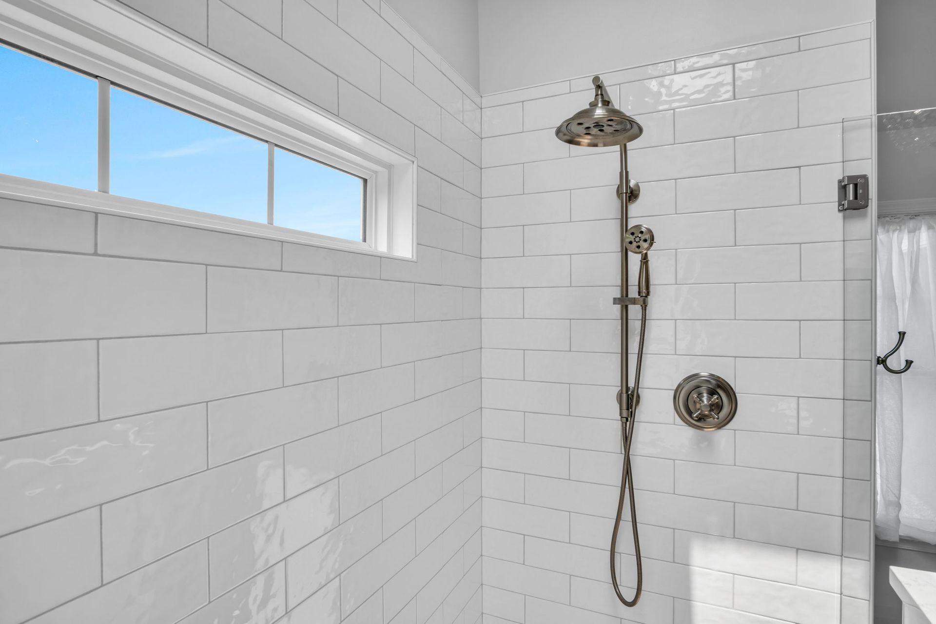 A bathroom with white tiles and a shower head.