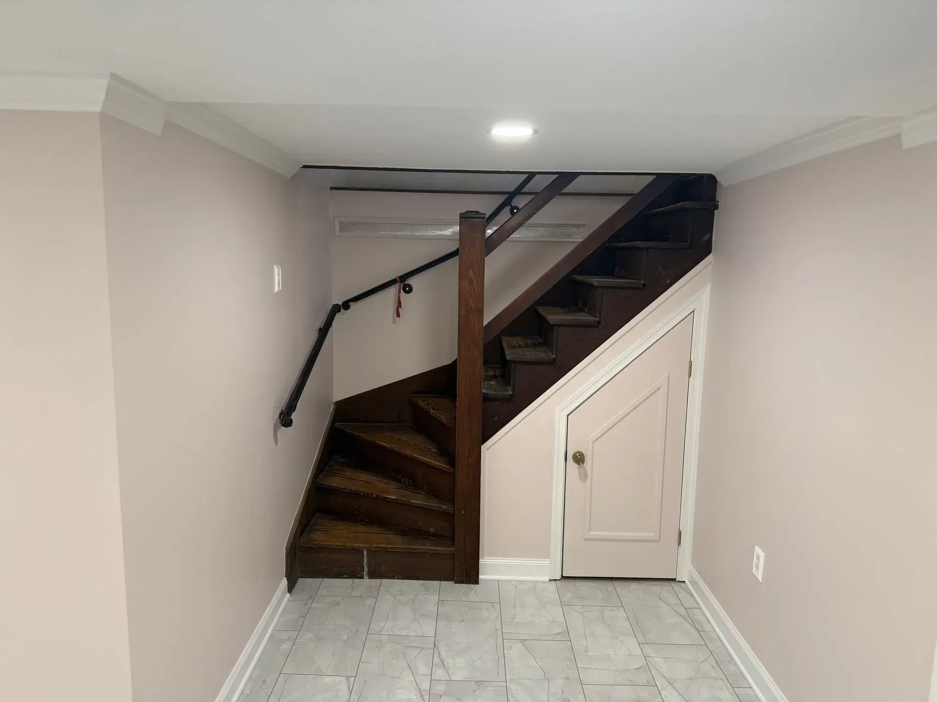 Staircase in room with pink walls, dark wood stairs, and a closed door underneath.