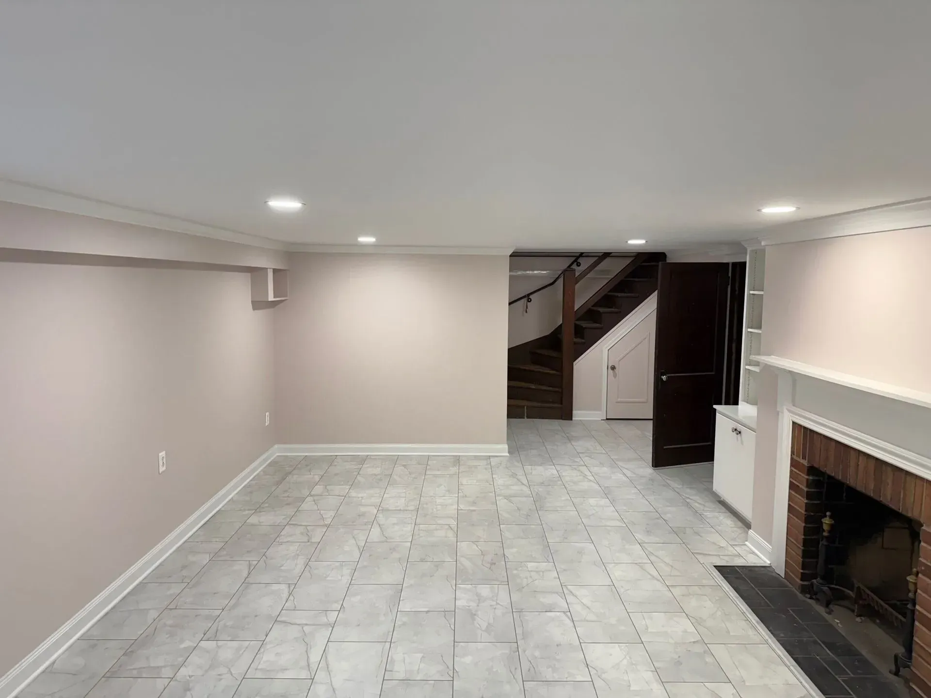 Basement room with pink walls, gray tiled floor, fireplace, and stairs.