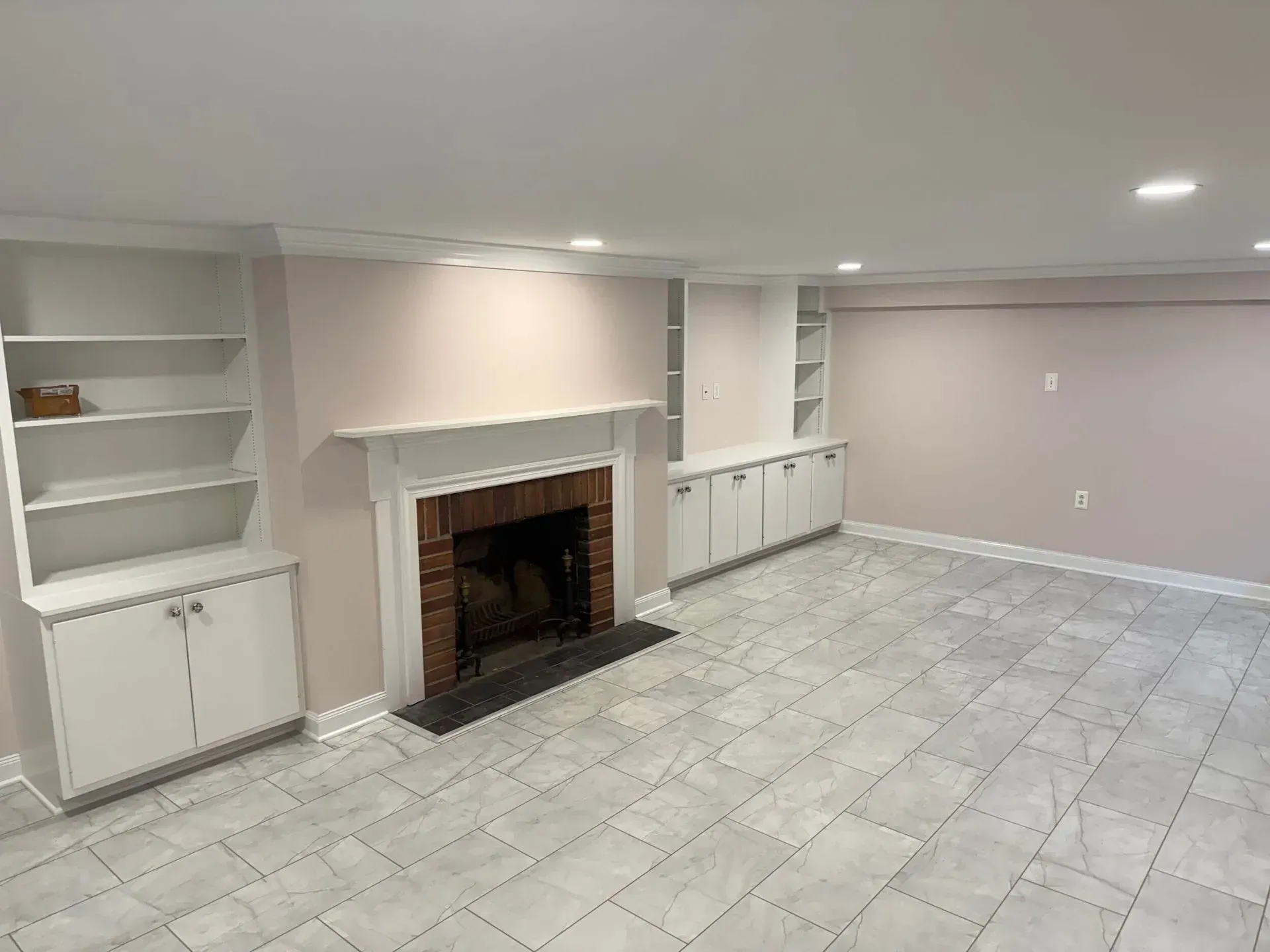 Empty room with fireplace, white shelves, and light gray tiled floor.