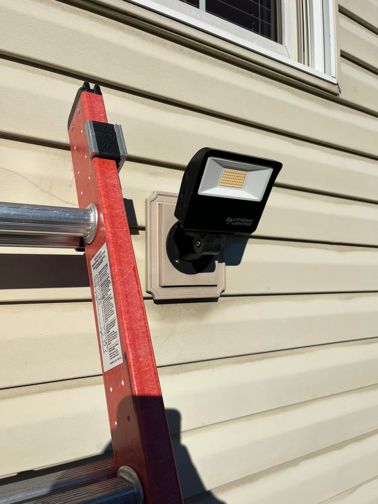 A ladder is attached to a light on the side of a house.
