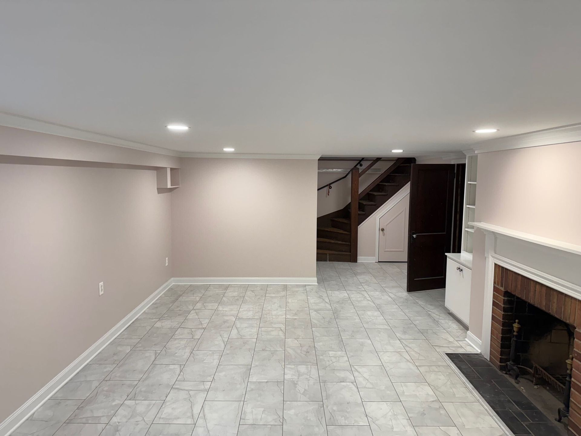 Empty basement with tiled floor, fireplace, stairs, and neutral walls.