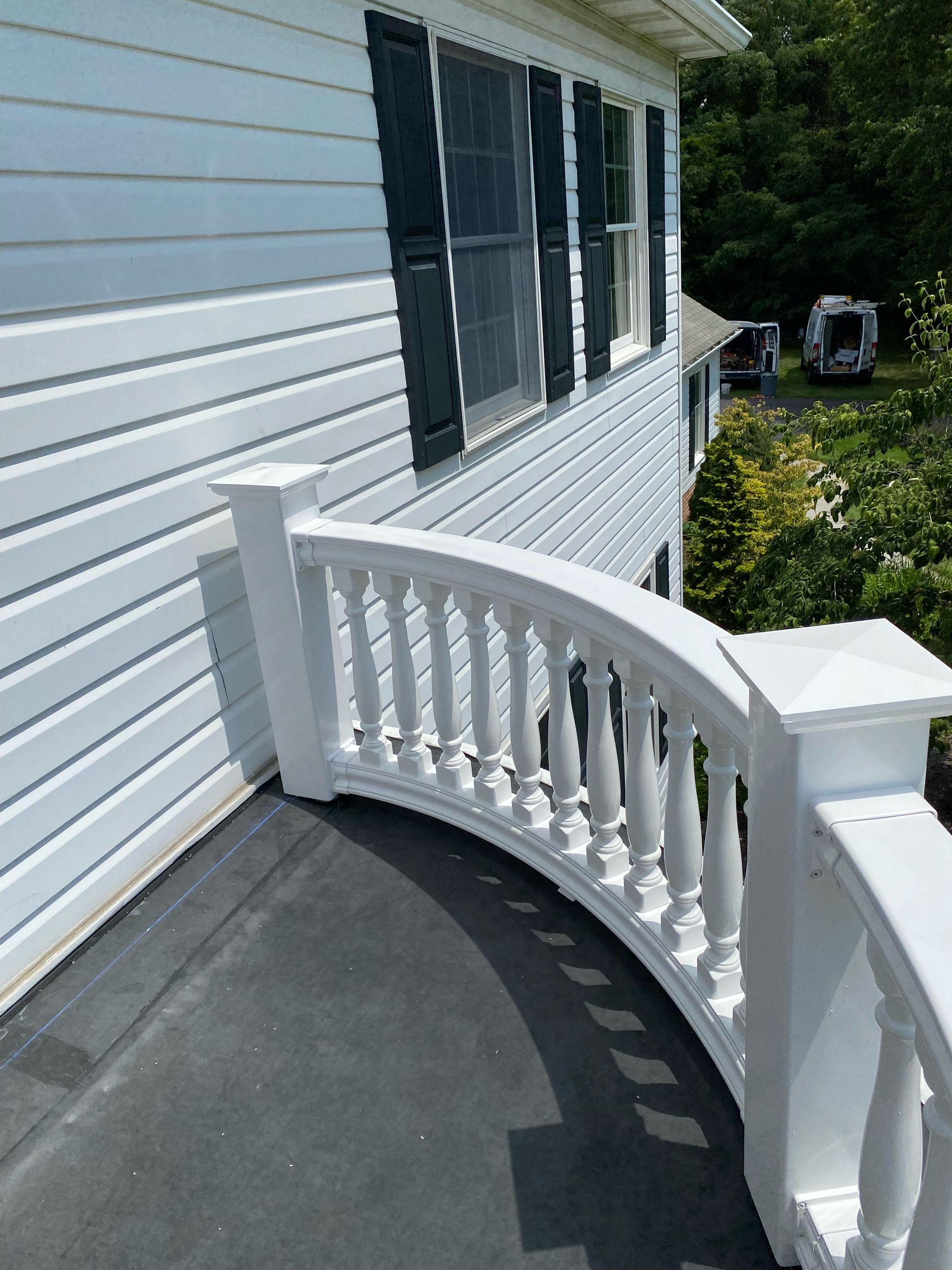 White balustrade curves around a porch on a house with white siding and black shutters.