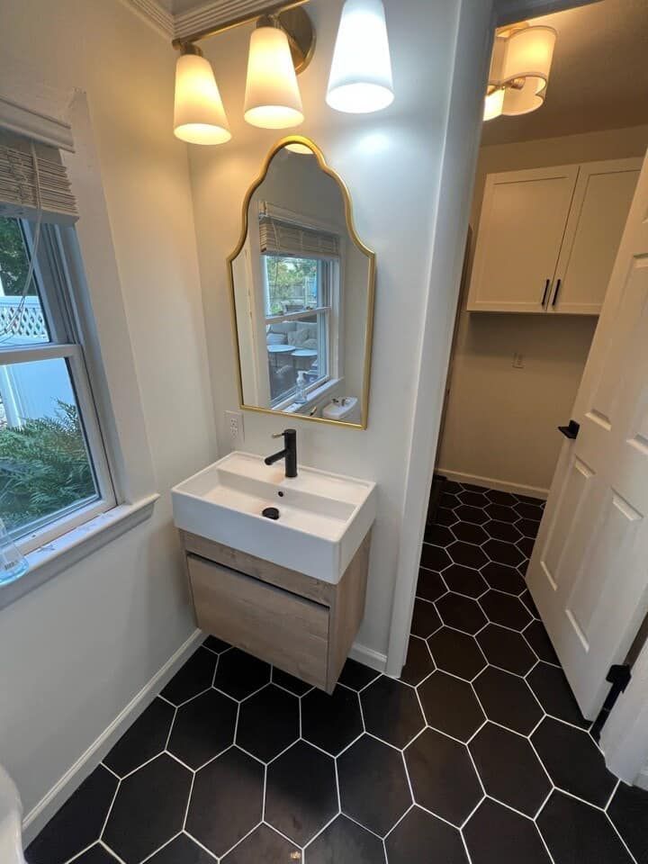 A bathroom with a sink , mirror , and black tile floor.