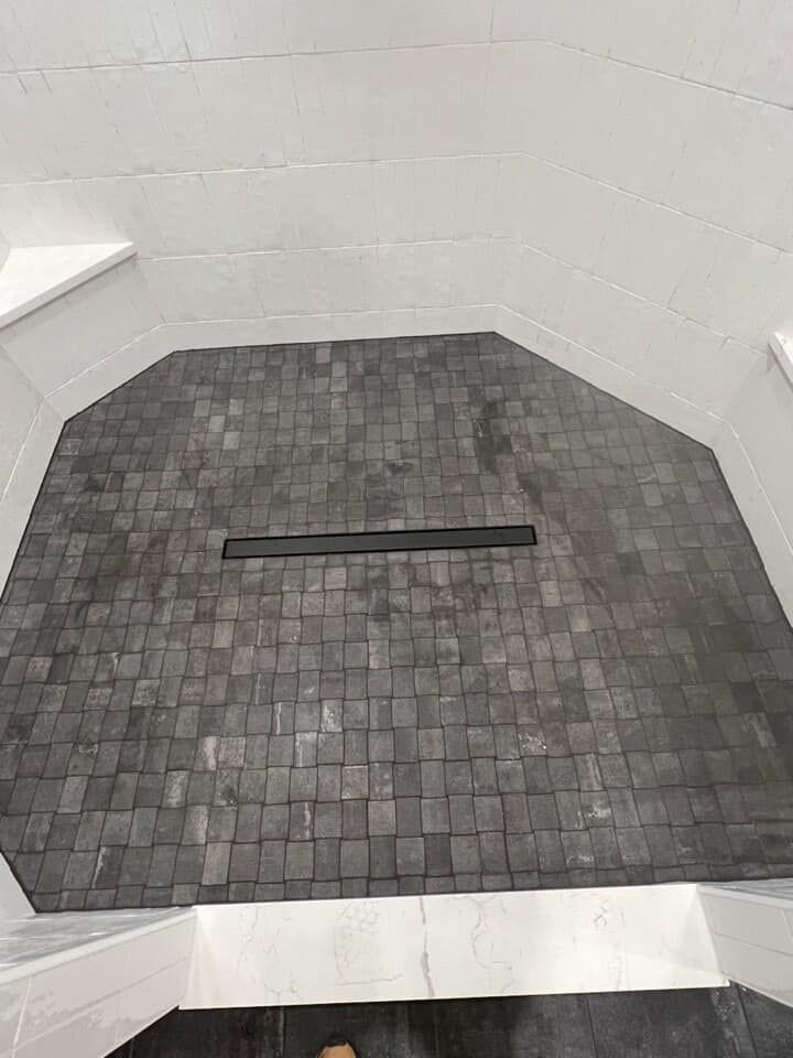 A black and white photo of a tiled shower floor with a drain.