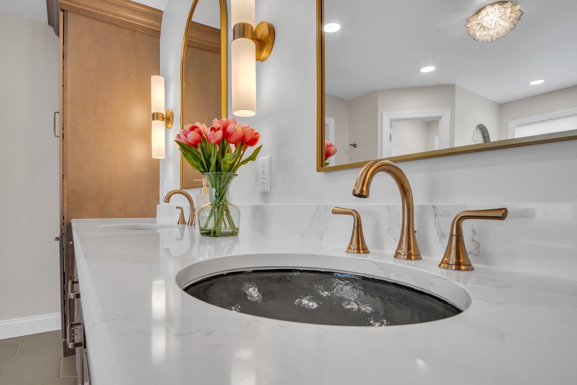 A bathroom with a sink , mirror and vase of flowers.