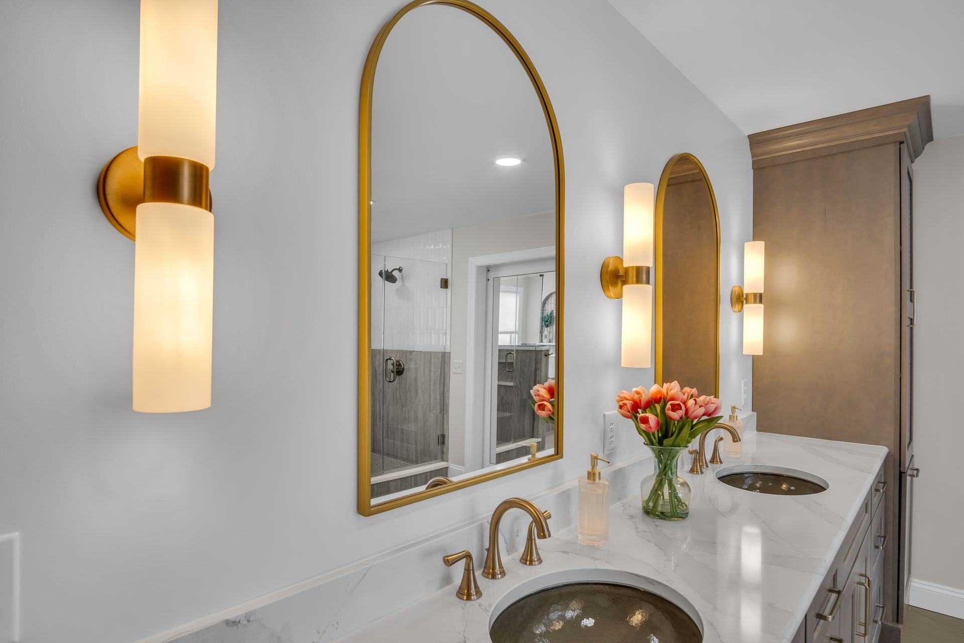 A bathroom with two sinks , two mirrors and two lights.