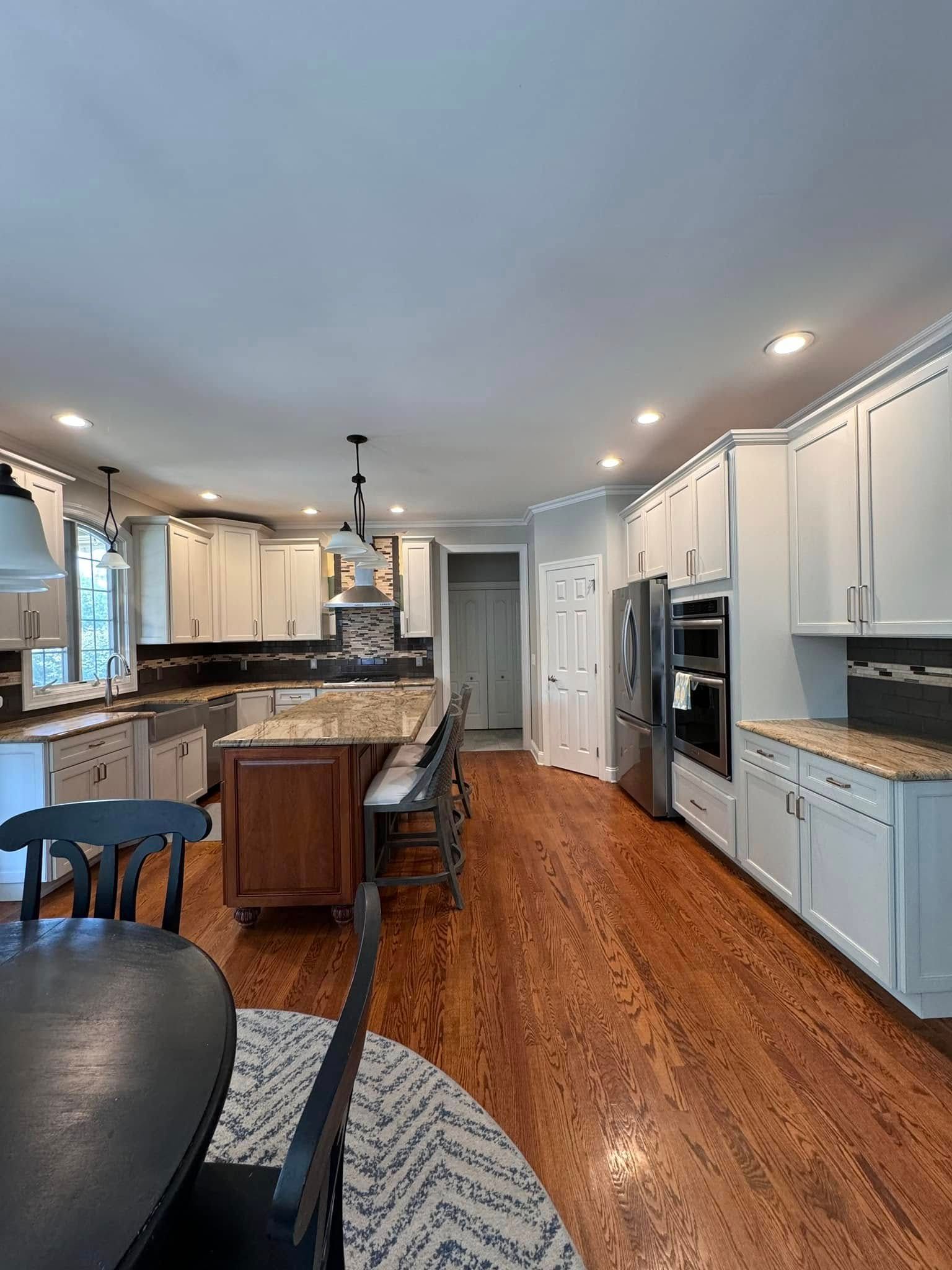 A kitchen with white cabinets , granite counter tops , stainless steel appliances and hardwood floors.