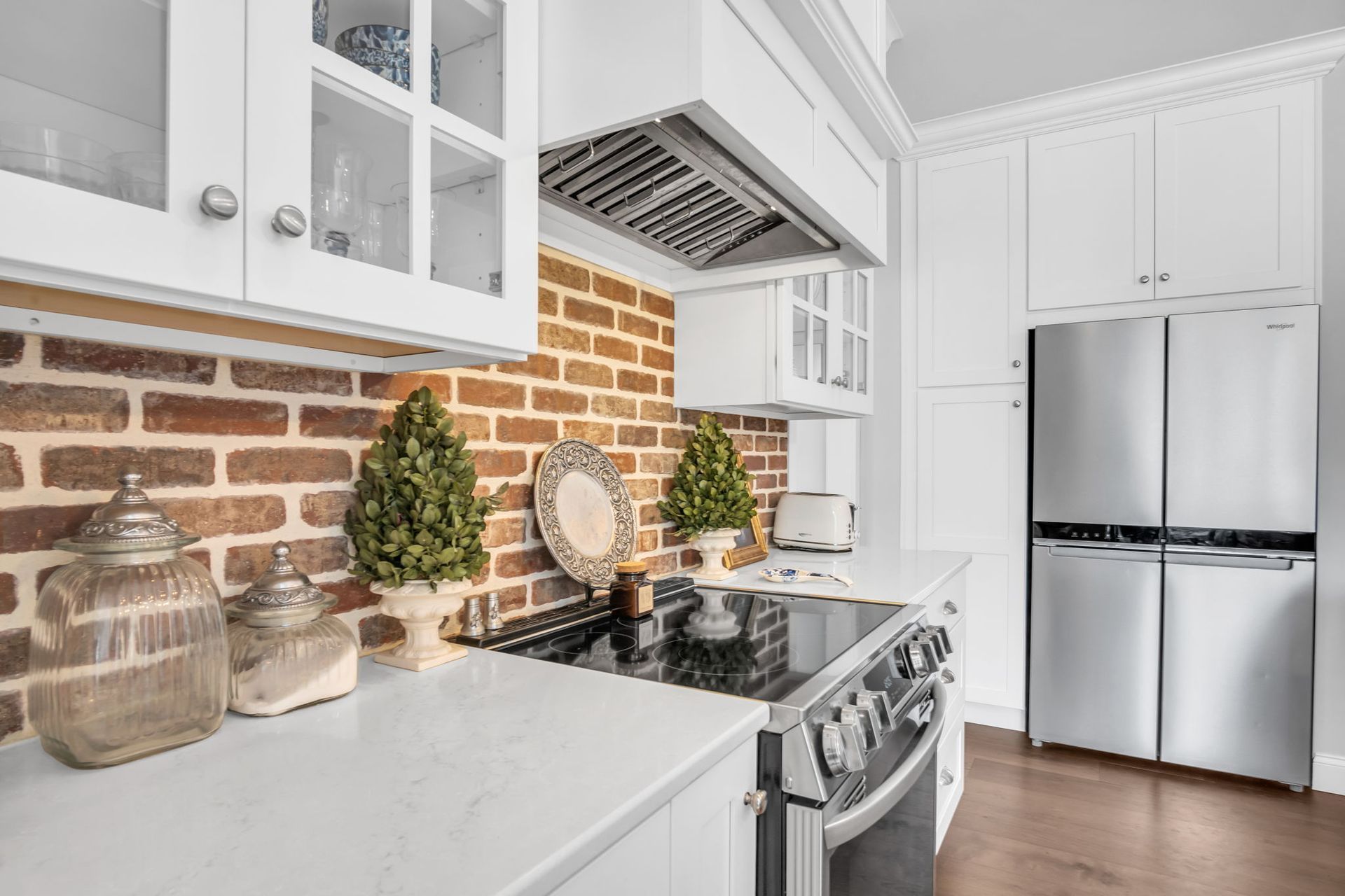 A kitchen with white cabinets , a stove , a refrigerator , and a brick wall.
