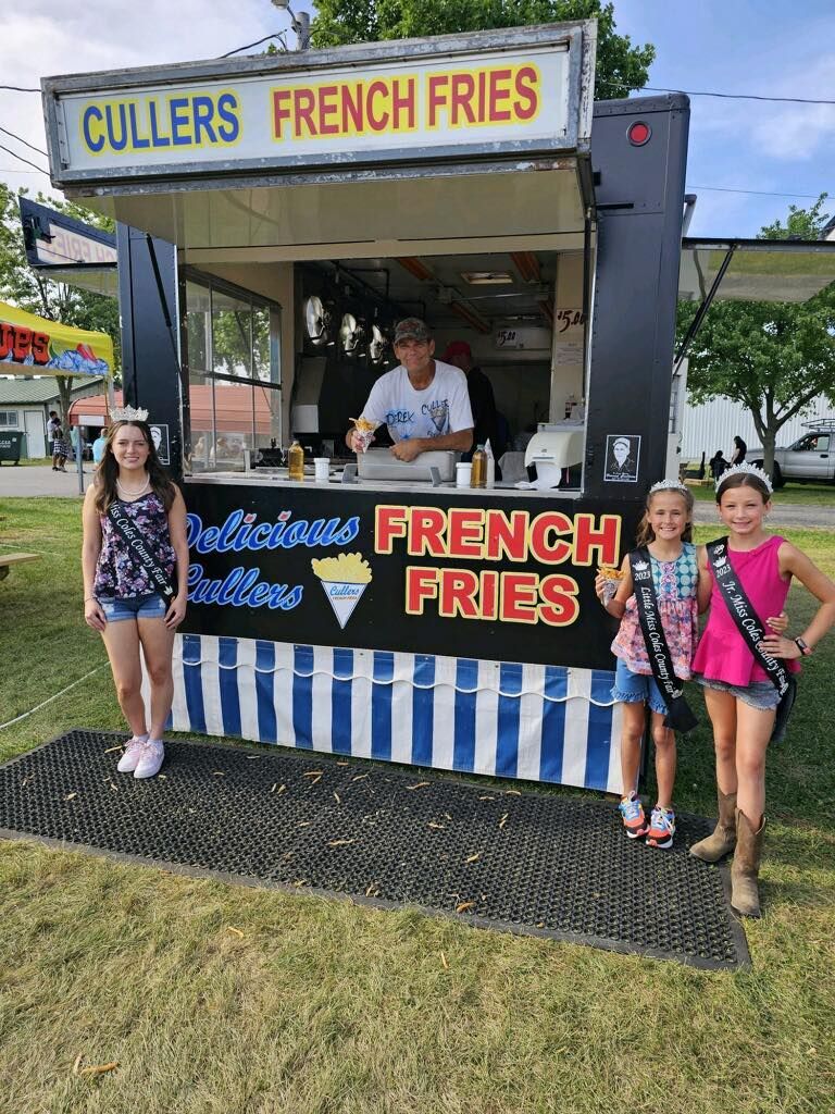 A group of young girls are standing in front of a french fries stand.