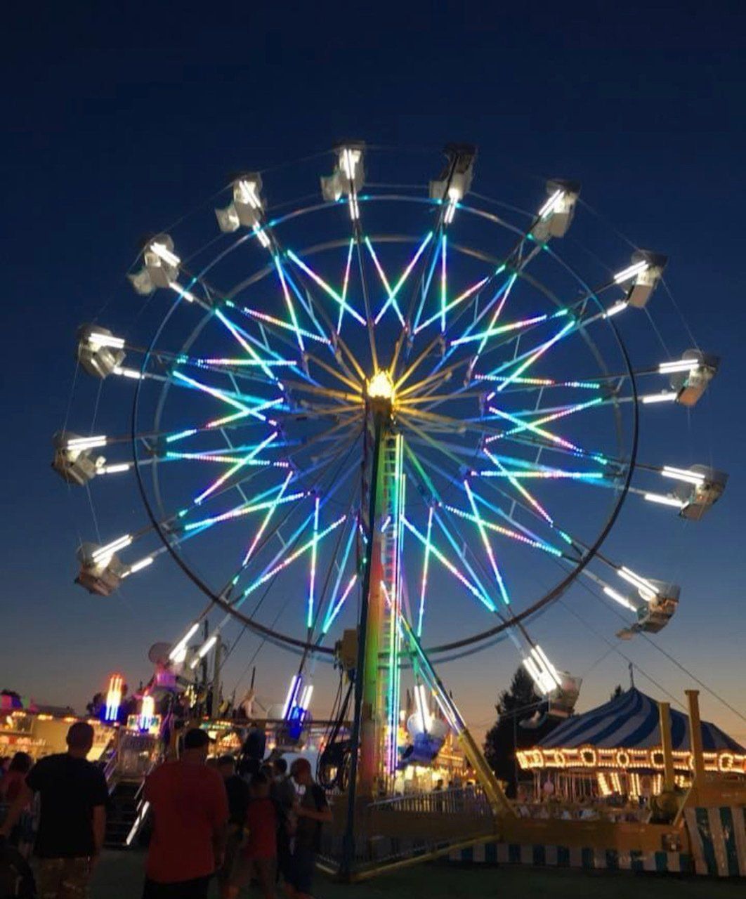 A ferris wheel is lit up at a carnival at night