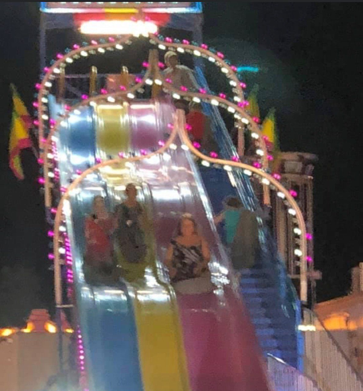 A group of people are riding a slide at a carnival at night.
