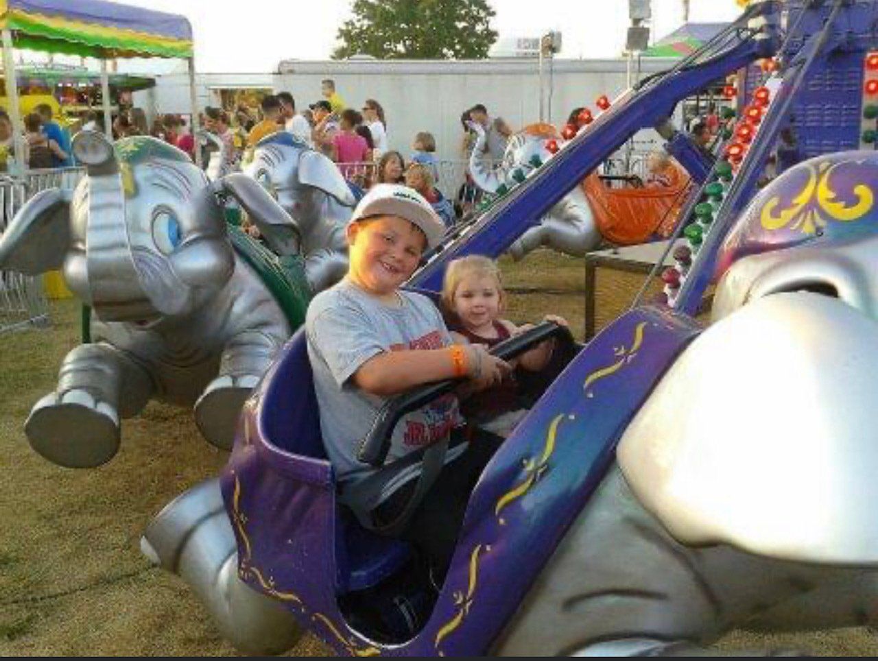 A boy and a little girl are riding an elephant ride at a carnival