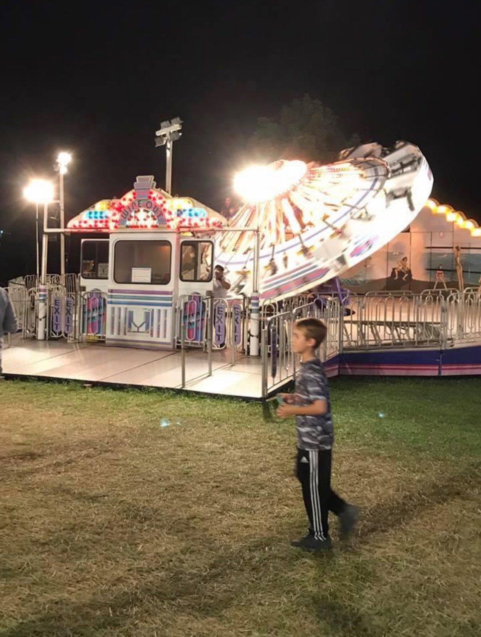 A boy standing in front of a carnival ride at night