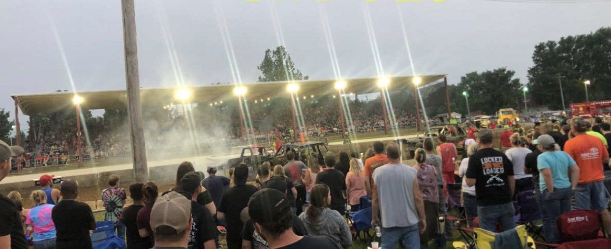 A crowd of people are standing in front of a stadium watching a race.
