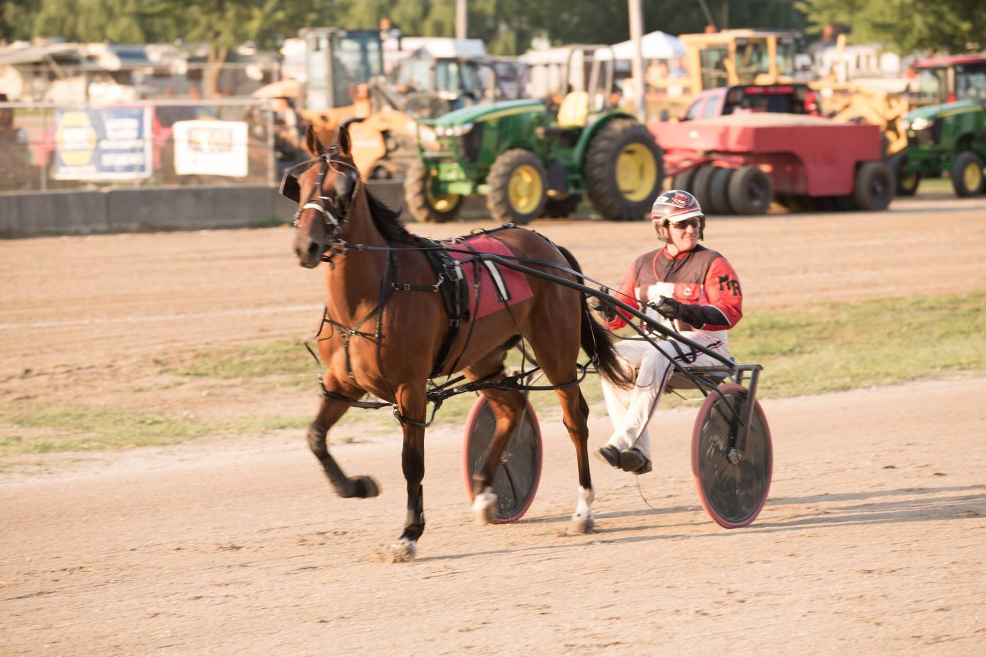 A man is riding a horse drawn carriage on a dirt track.