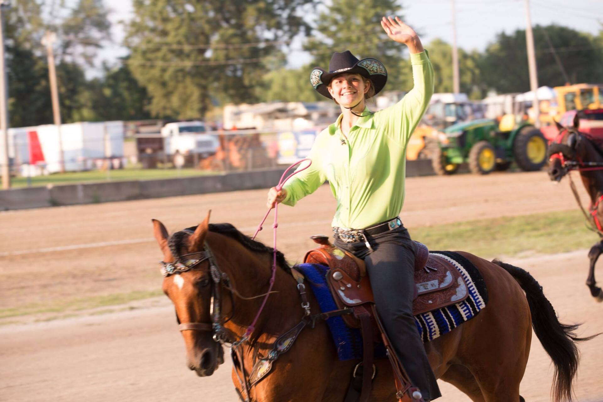 A woman is riding a horse and waving at the camera.
