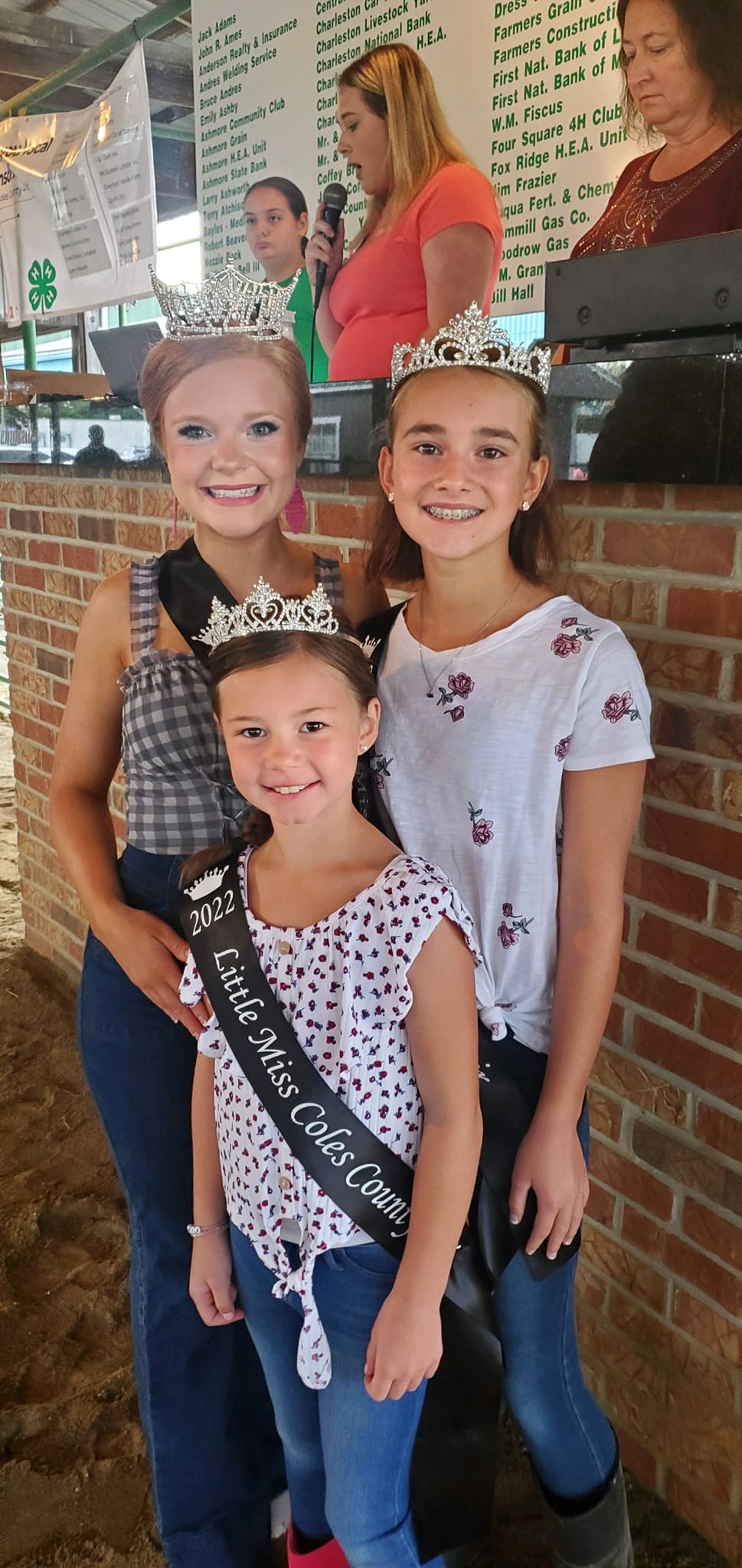 Three young girls wearing crowns and sashes are posing for a picture.