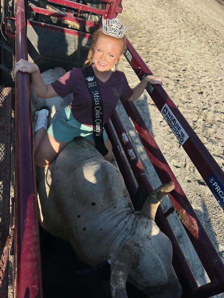 A little girl is sitting on a bull wearing a sash that says miss rodeo