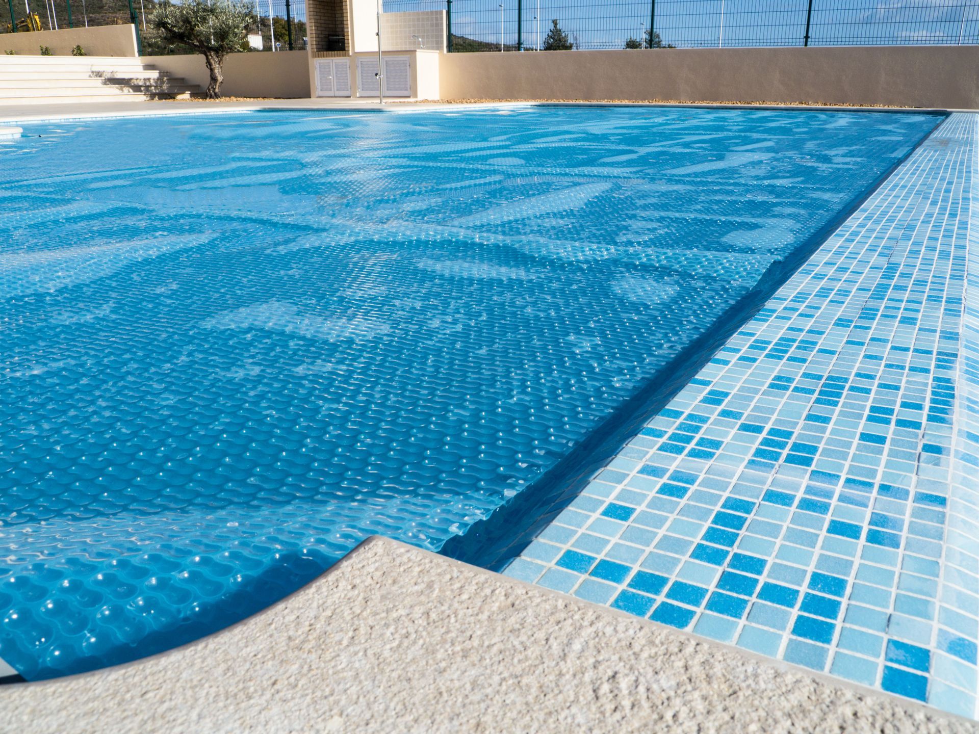 Blue solar pool cover on a pool with blue and white tile trim.