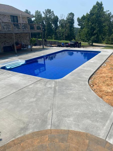 Rectangular swimming pool with blue water and concrete patio, next to a house with a deck.
