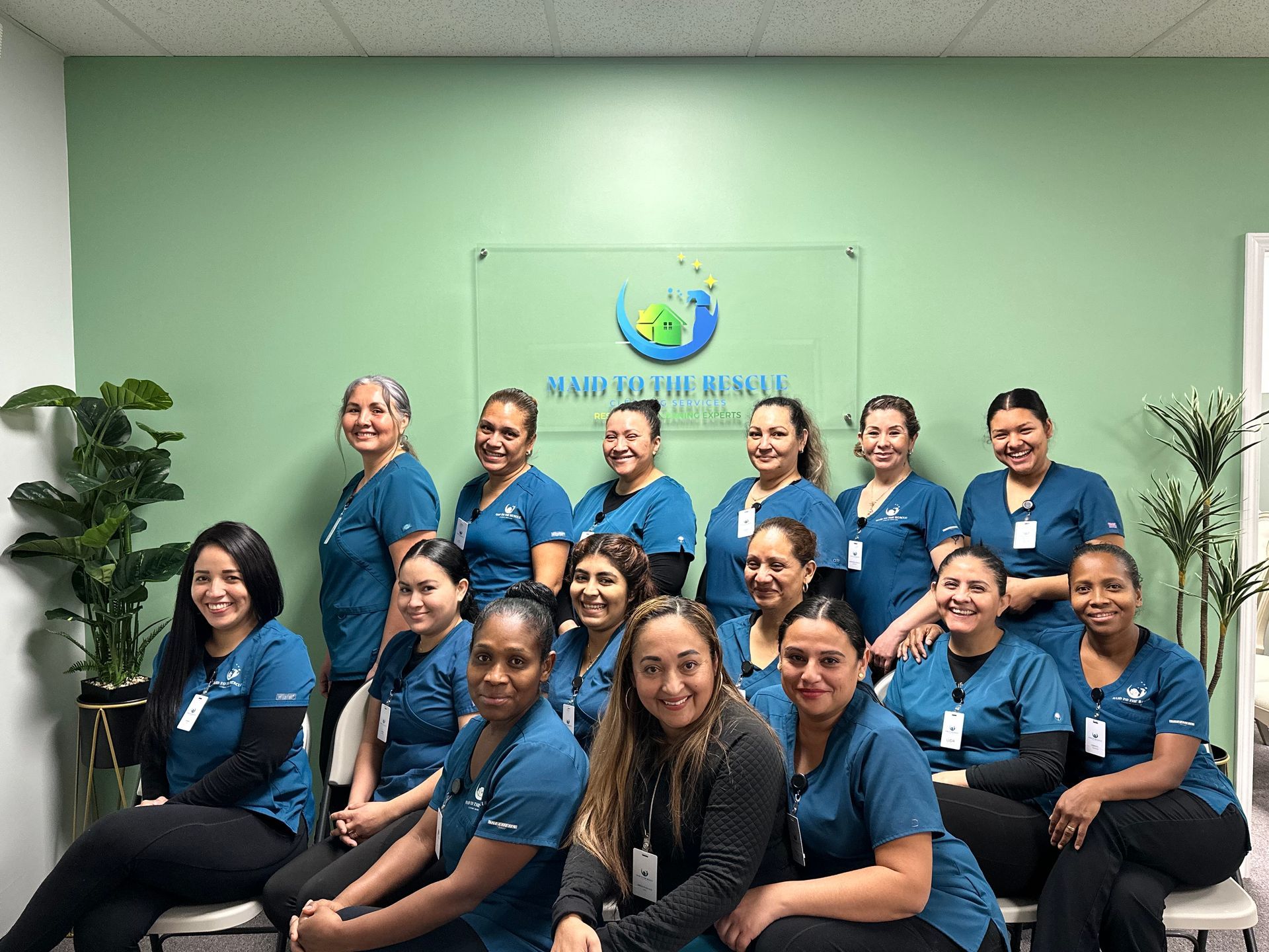 A group of staff members in blue scrubs posing in front of a green wall with the 