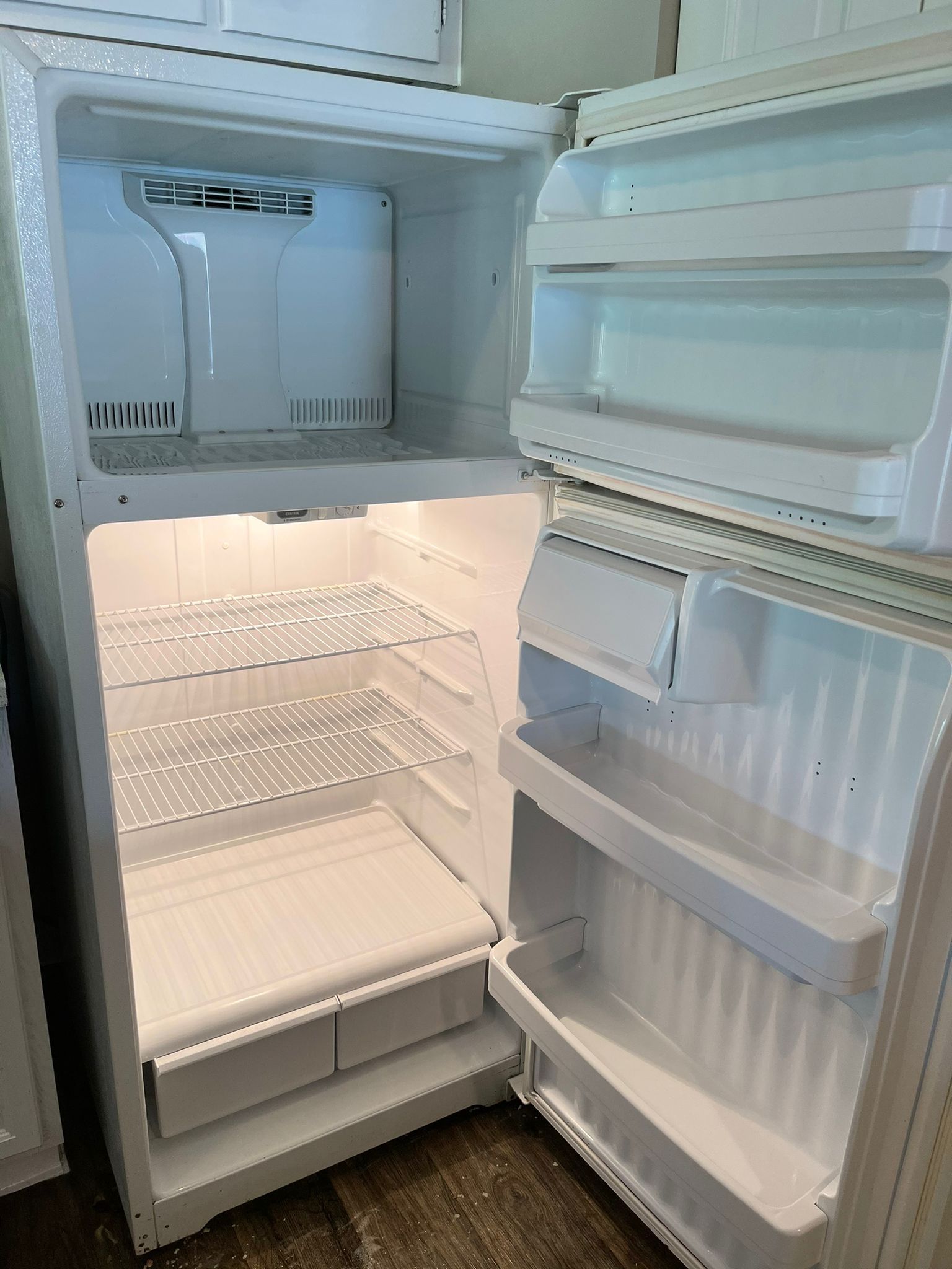 An empty, clean white top-freezer refrigerator with shelves and door bins, standing in a room.