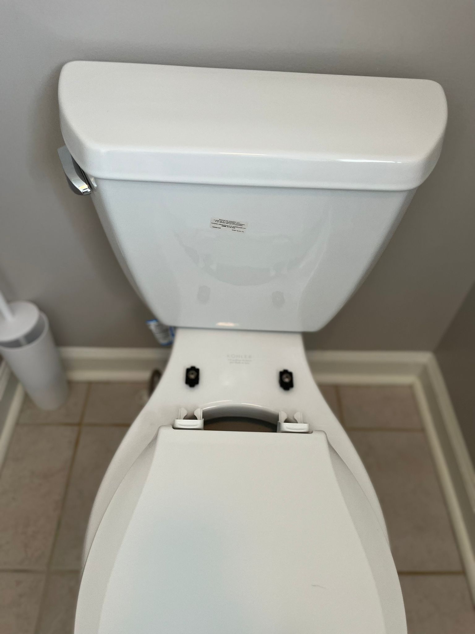 A top-down view of a white ceramic toilet with the seat down, positioned against a light gray wall on a tiled floor.