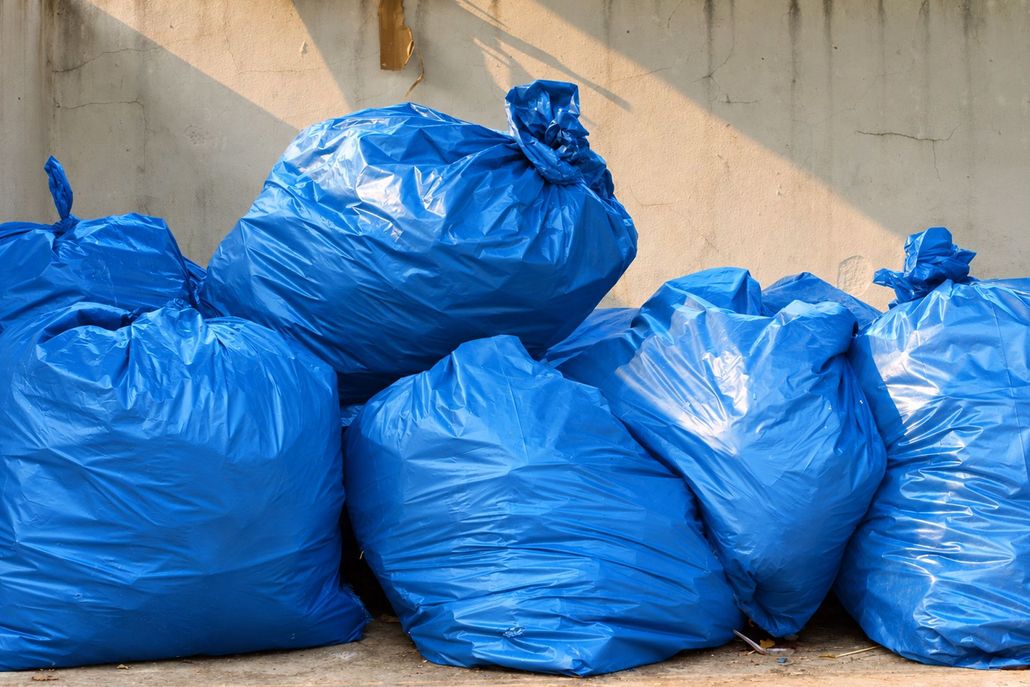 Blue garbage bags piled against a concrete wall.