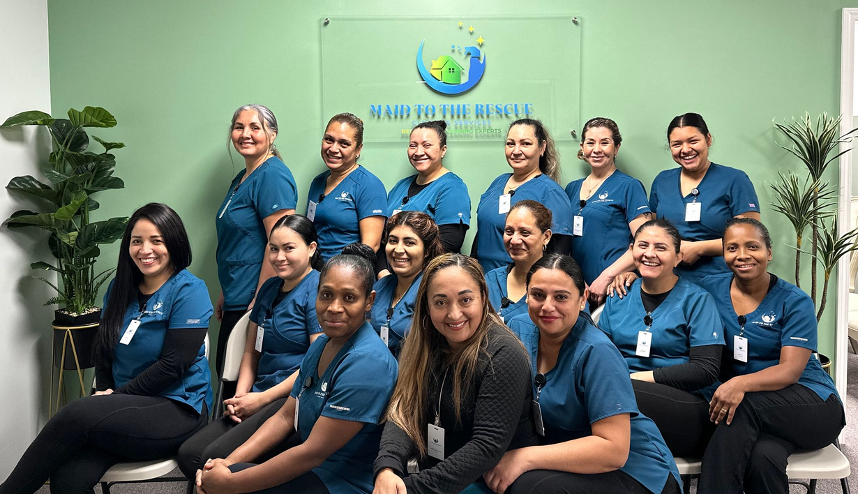 A group of healthcare workers in blue scrubs posing for a photo in front of a clinic logo against a green wall.