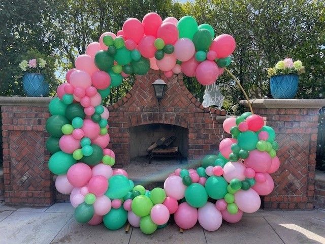 A bunch of pink and green balloons are sitting in front of a fireplace.