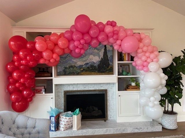 A living room with a fireplace decorated with pink and red balloons.