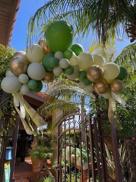 A bunch of green and gold balloons are hanging over a gate.