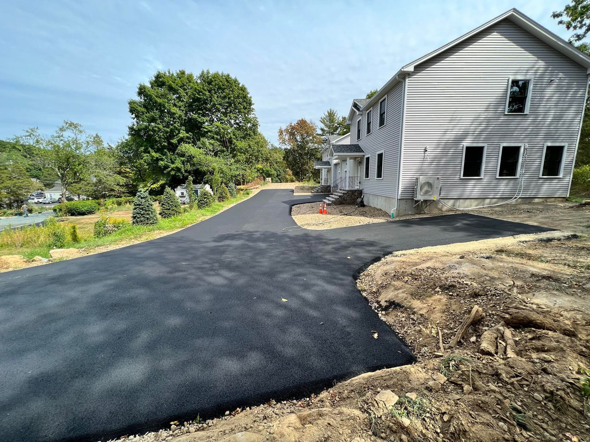 Newly paved black driveway beside a gray house on a sunny day
