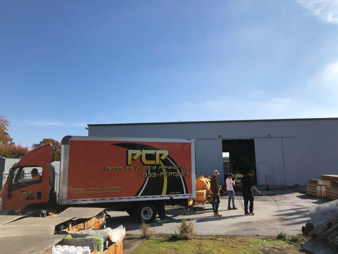 Red PCR delivery truck parked by a warehouse with two people standing nearby under a blue sky