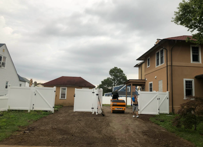 Open gate at a house driveway with a worker and orange utility cart under cloudy sky