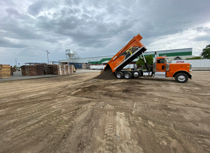 Orange dump truck unloading dirt at a construction site under a cloudy sky