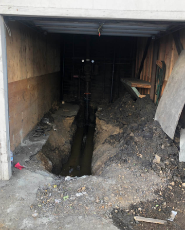 Open garage with a deep trench dug through the dirt floor and tools along the sides.