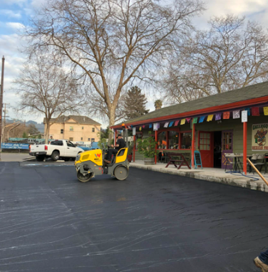 Yellow forklift parked outside a storefront with colorful bunting and a white truck nearby.