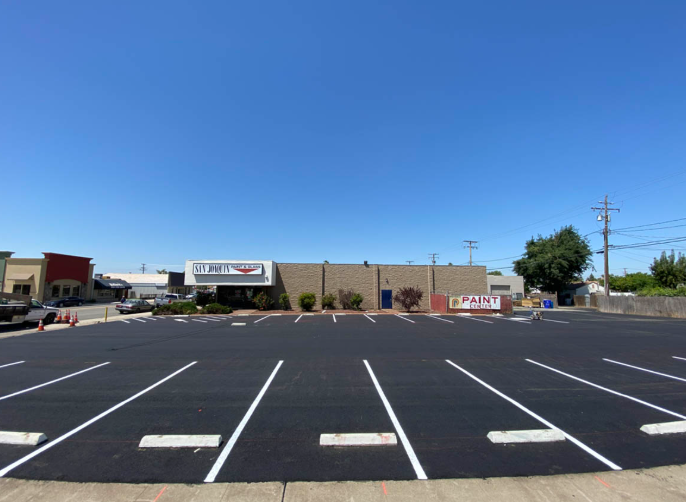 Empty parking lot outside a low-rise commercial building under a clear blue sky.