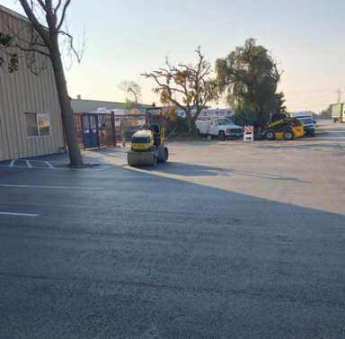 Parking lot with construction equipment, including a compact loader and utility vehicle, beside a building at sunset