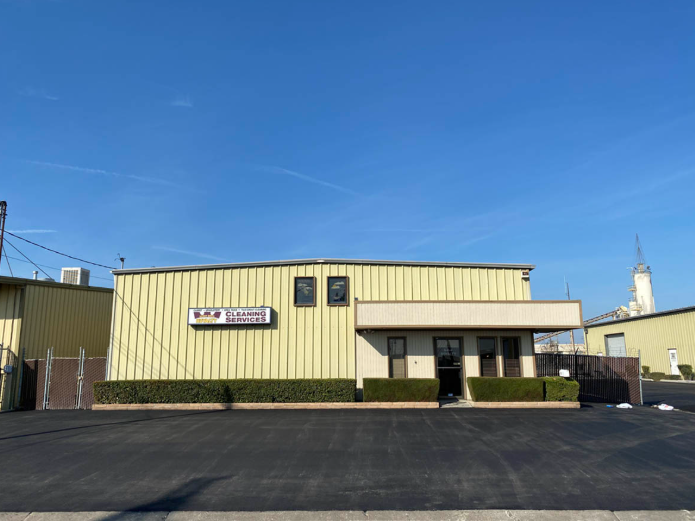 Yellow industrial building with a small sign and parking lot under a clear blue sky